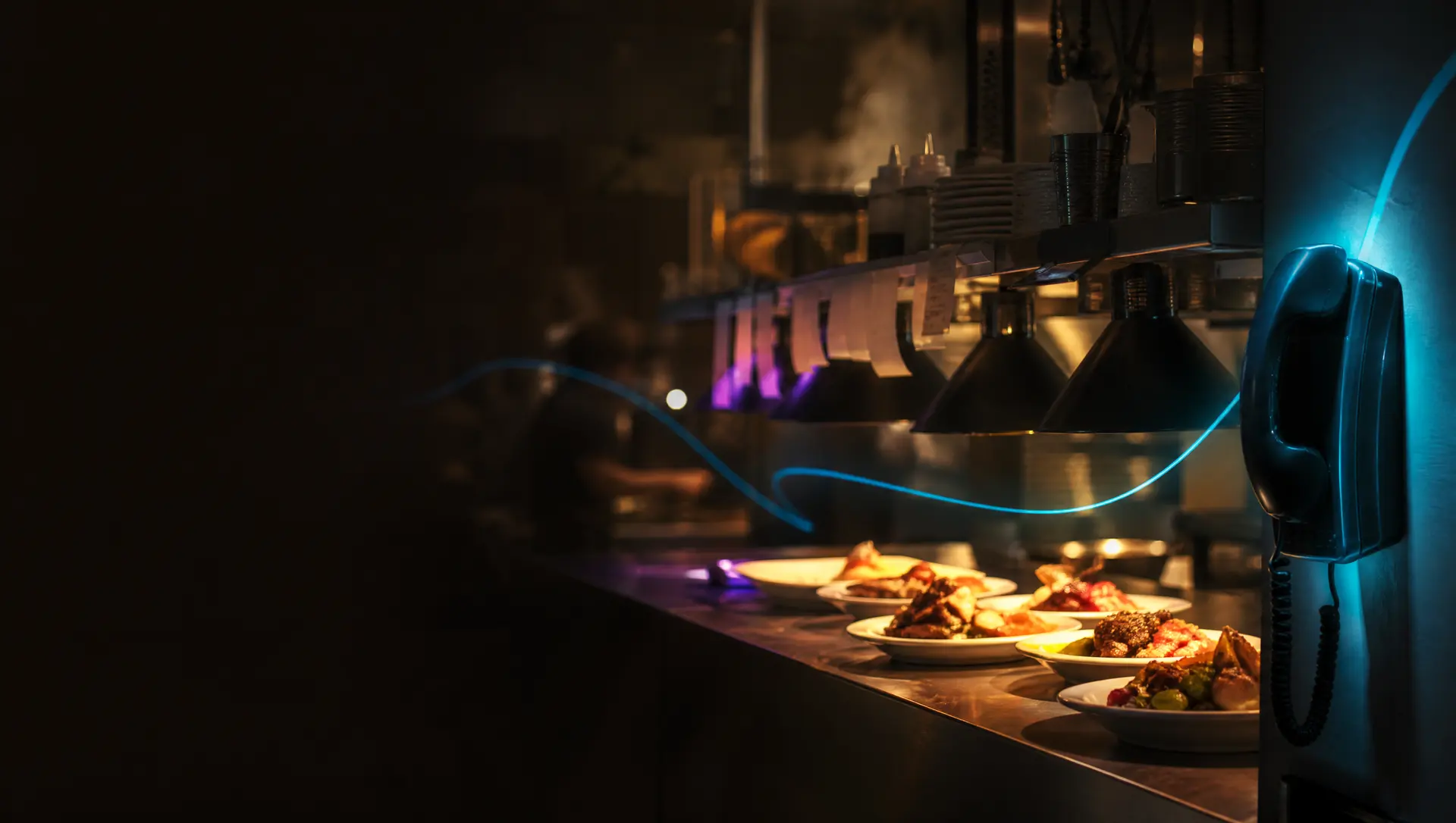 A busy restaurant kitchen pass with plated dishes and a wall phone glowing teal as an order is taken
